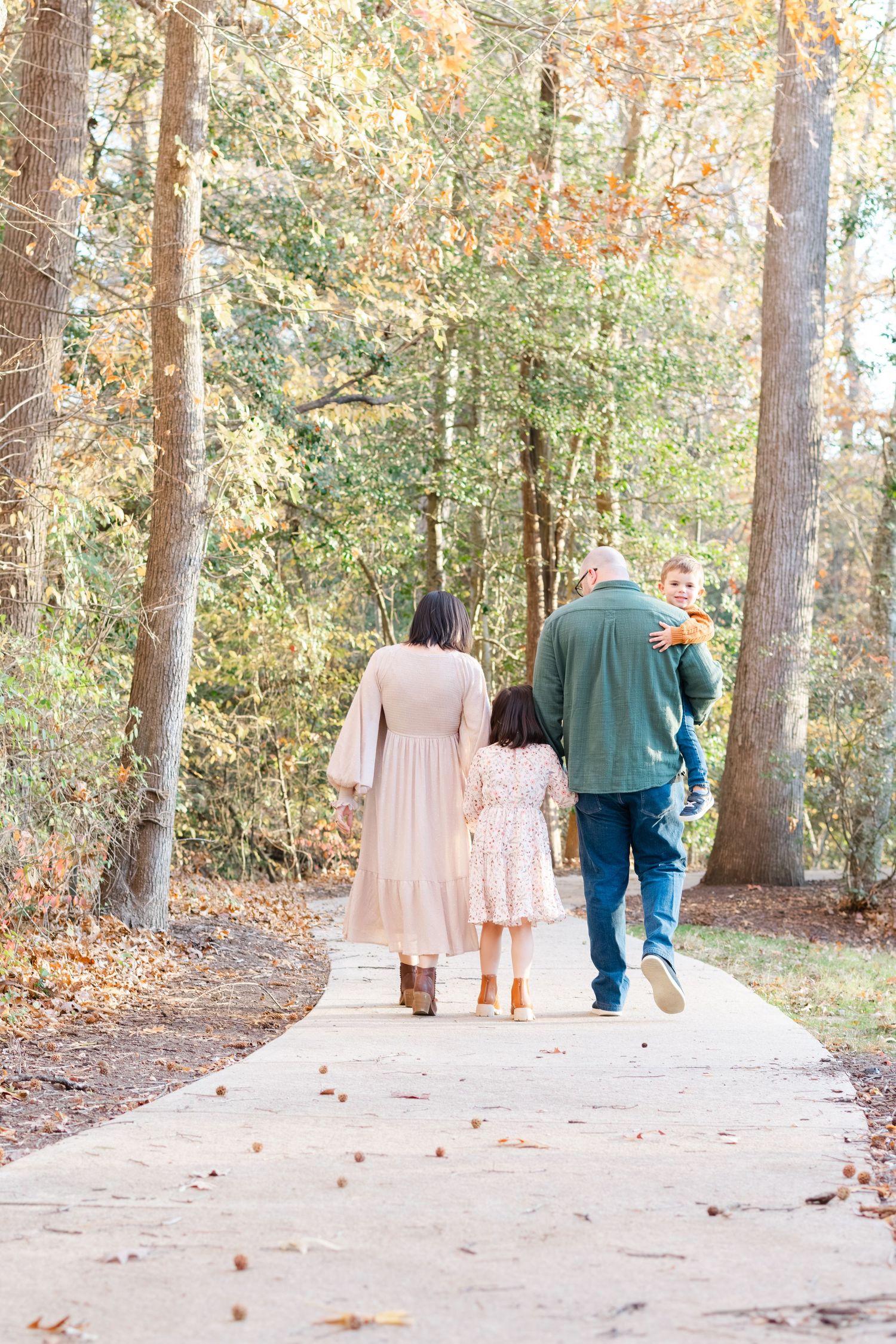 Family of four walking away on a tree-lined path in autumn, parents and two children enjoying a fall day outdoors.