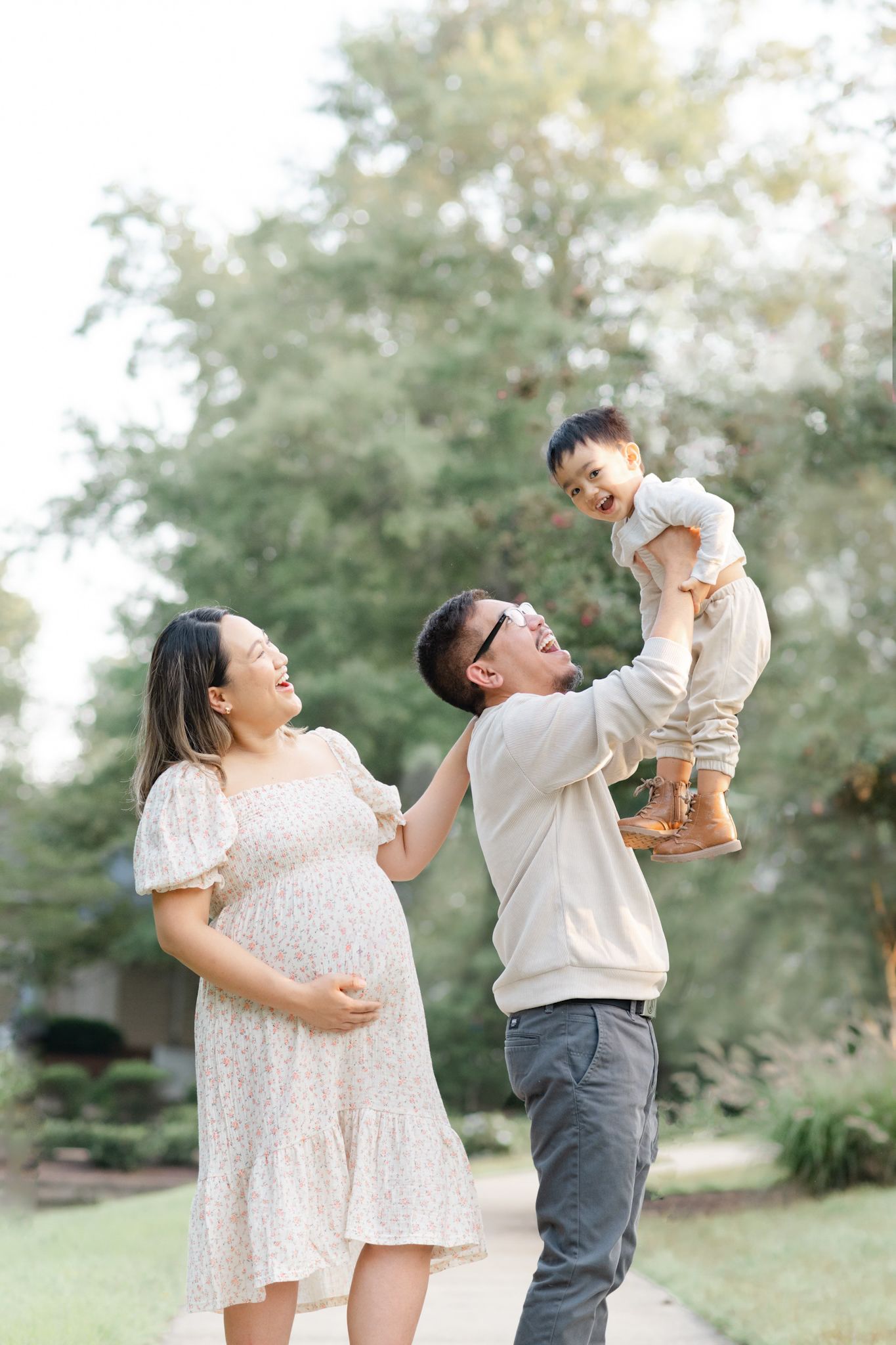 A family shares joyful moments together in a park setting with soft natural lighting and green foliage in the background.
