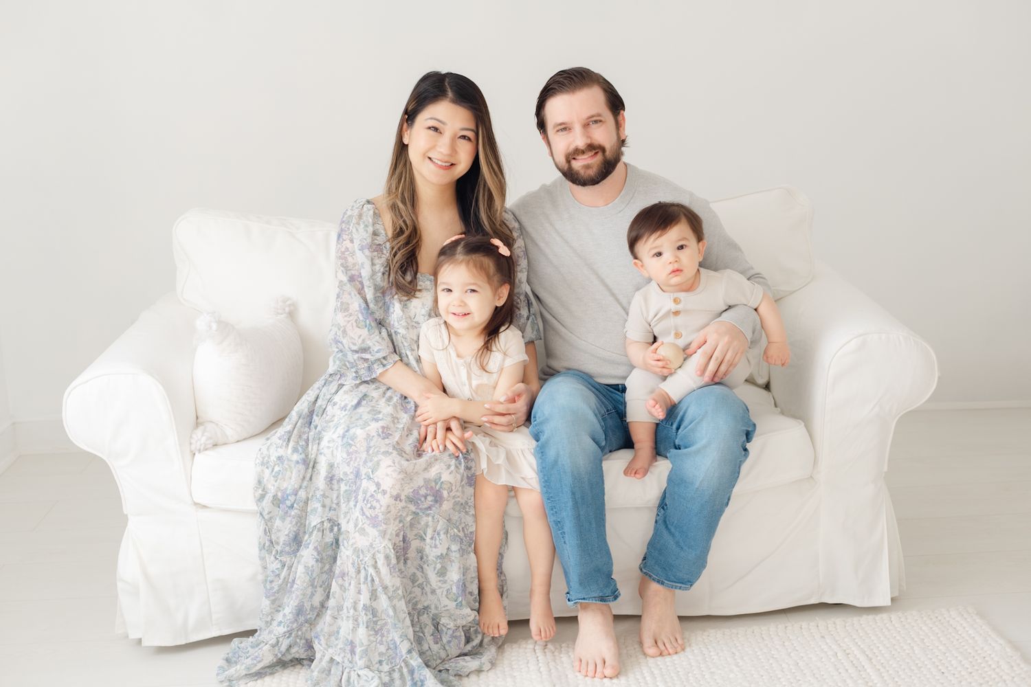 Family of four sitting together on white slipcovered couch.