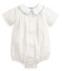 Vintage white cotton and lace baby dresses and christening gowns hang on display against a light background.