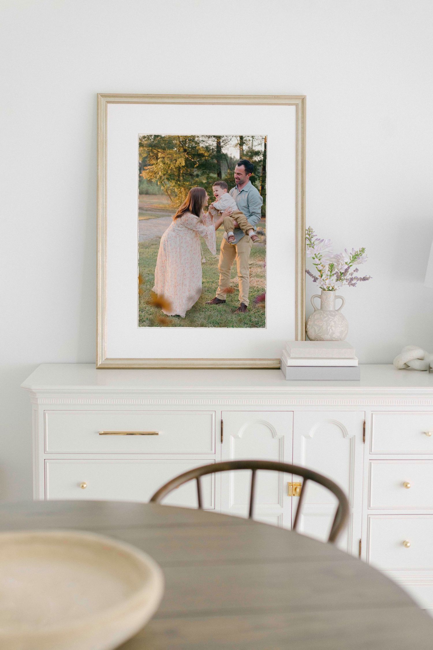 A minimalist white wall display with framed photos, decor items, and wooden furniture in a modern home interior setting.