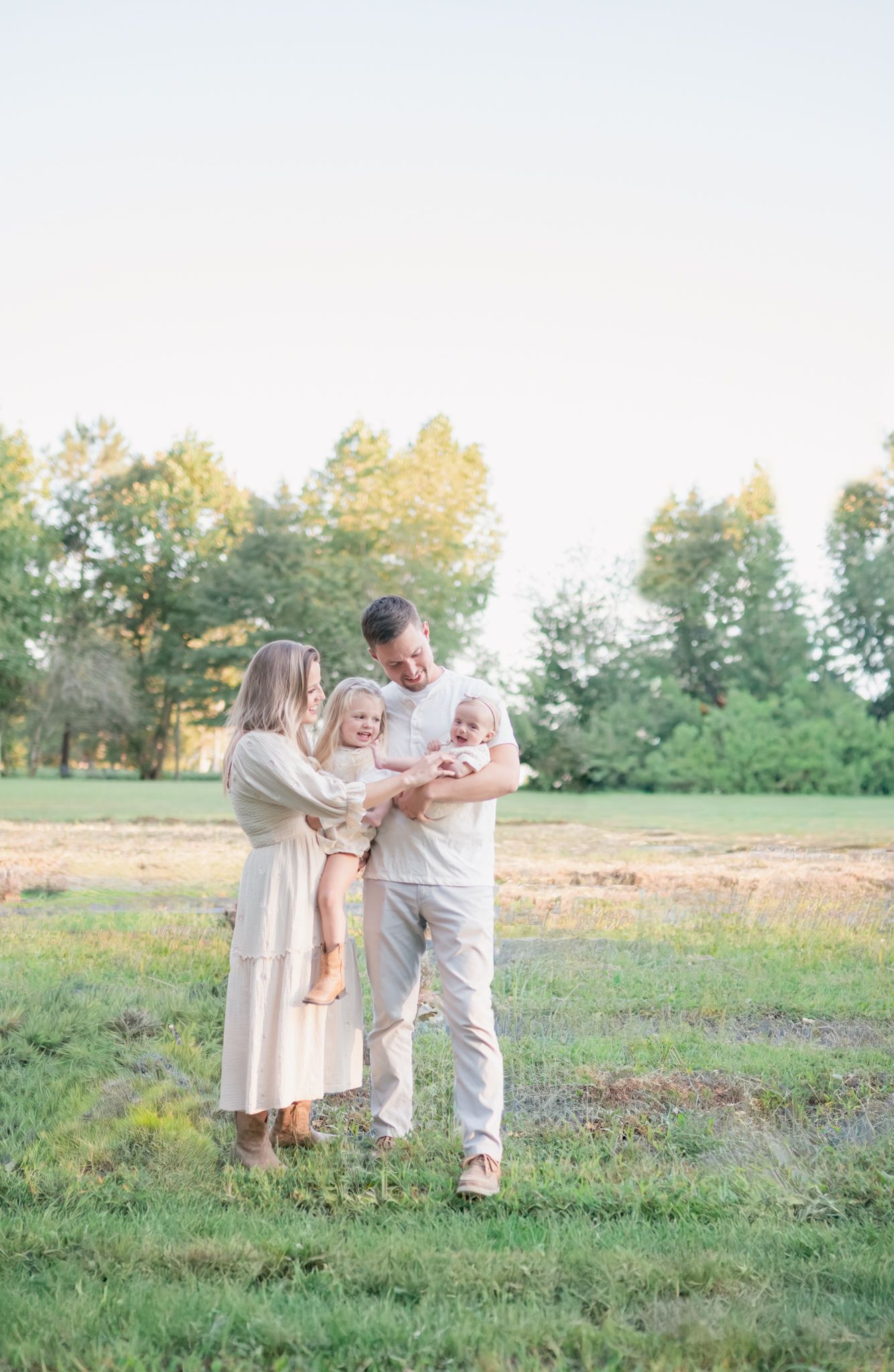 Family shares tender moment together while standing in sunlit grassy field.