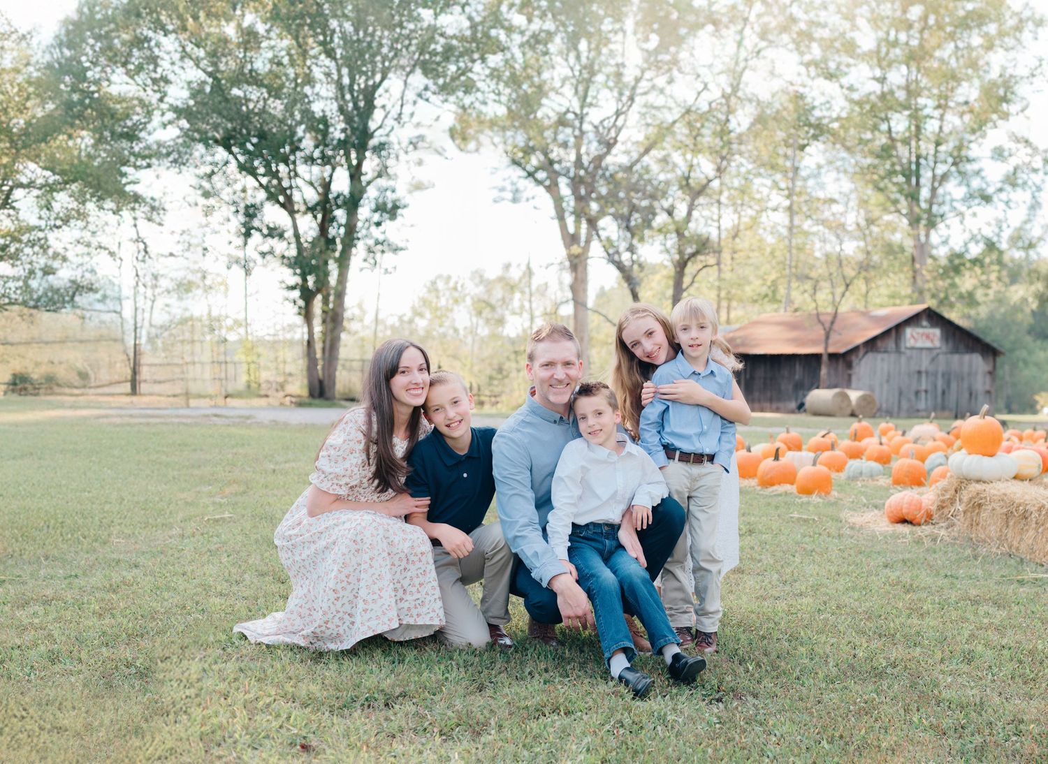 Happy family of five posing outdoors near pumpkins during fall season photo shoot.