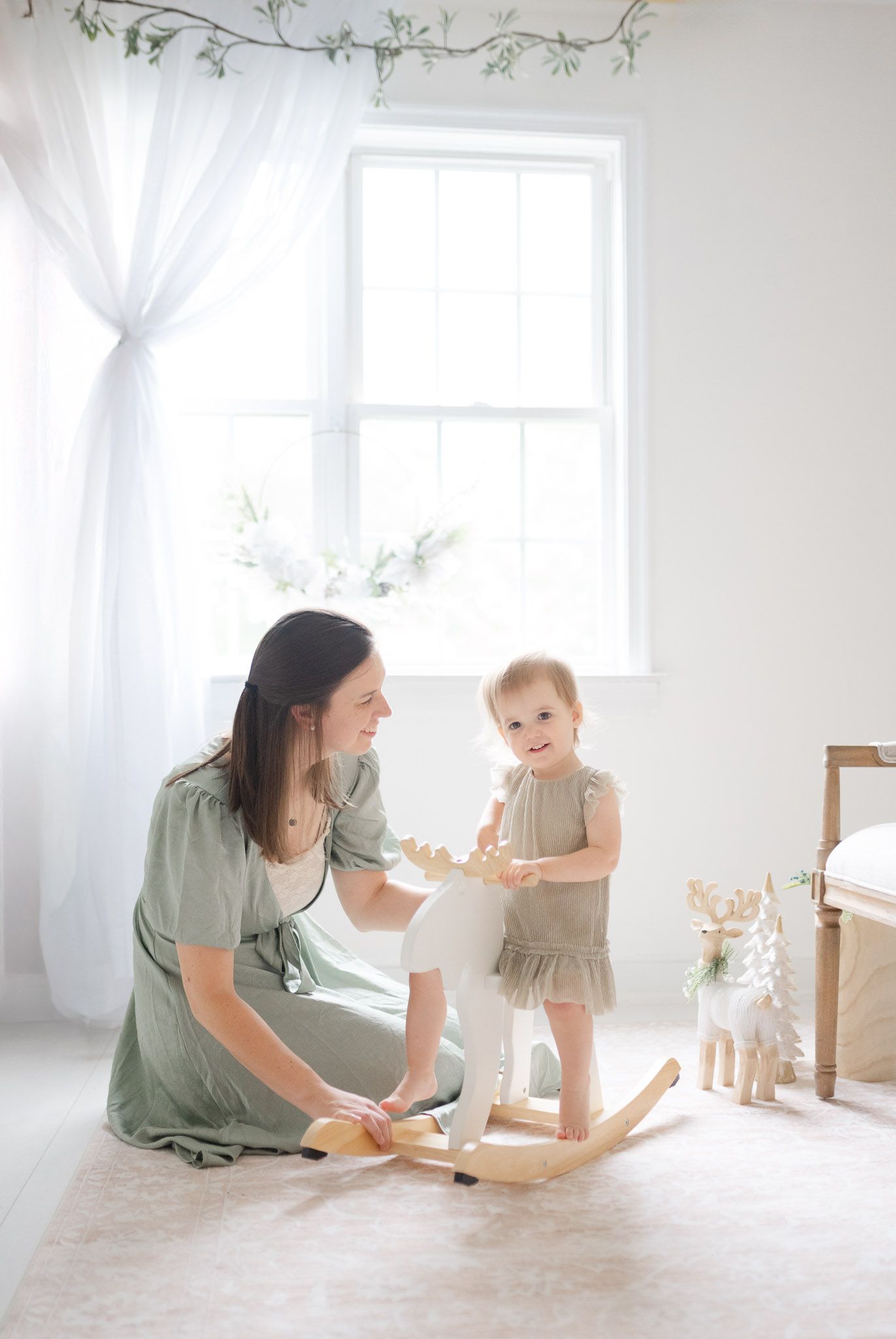 Parent and toddler playing together with wooden toys in a bright white minimalist room with soft natural lighting.