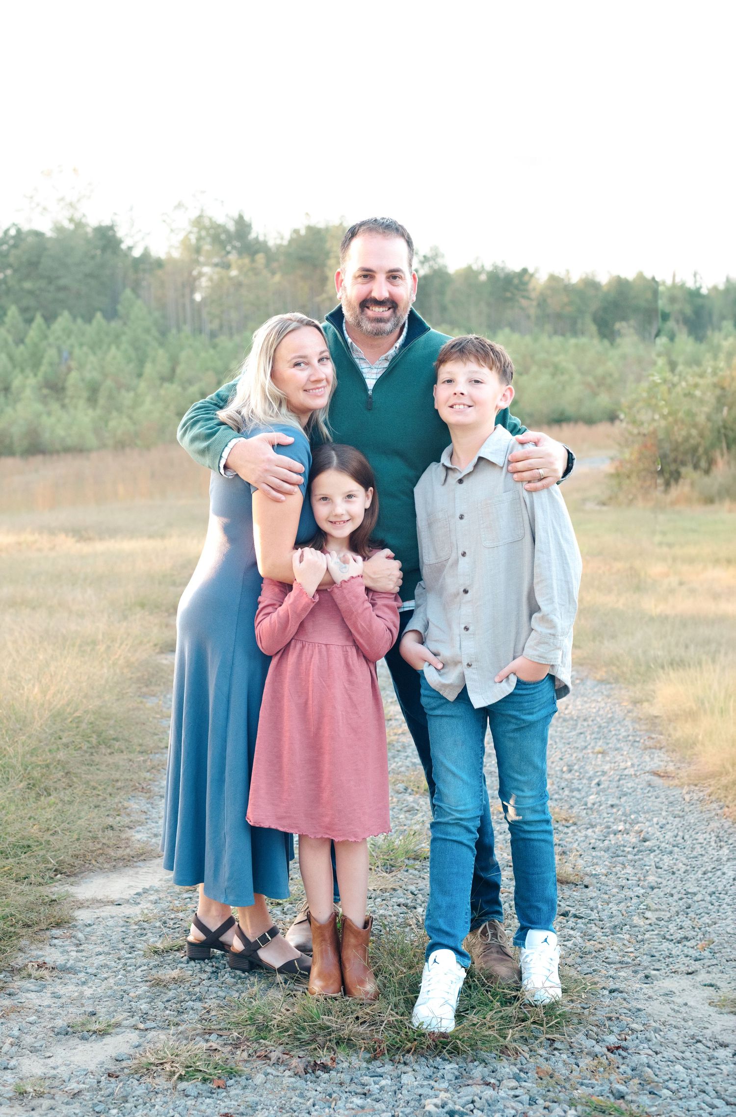 A happy family of four poses outdoors in a field, with parents and two children smiling in coordinated outfits.