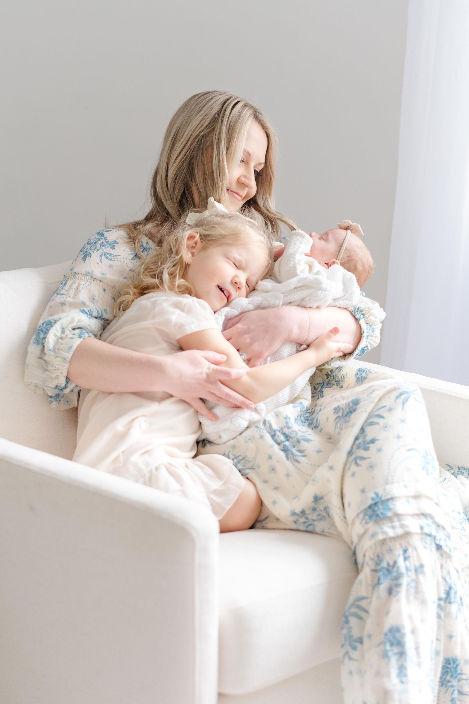 A woman in a floral dress relaxes on a white couch in a bright, minimalist setting.