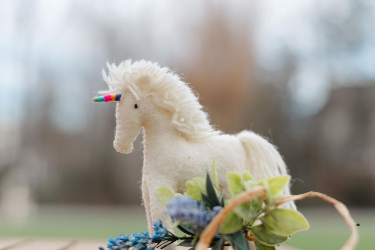 A small white puppy plays with green celery stalks while lying on a light colored surface.