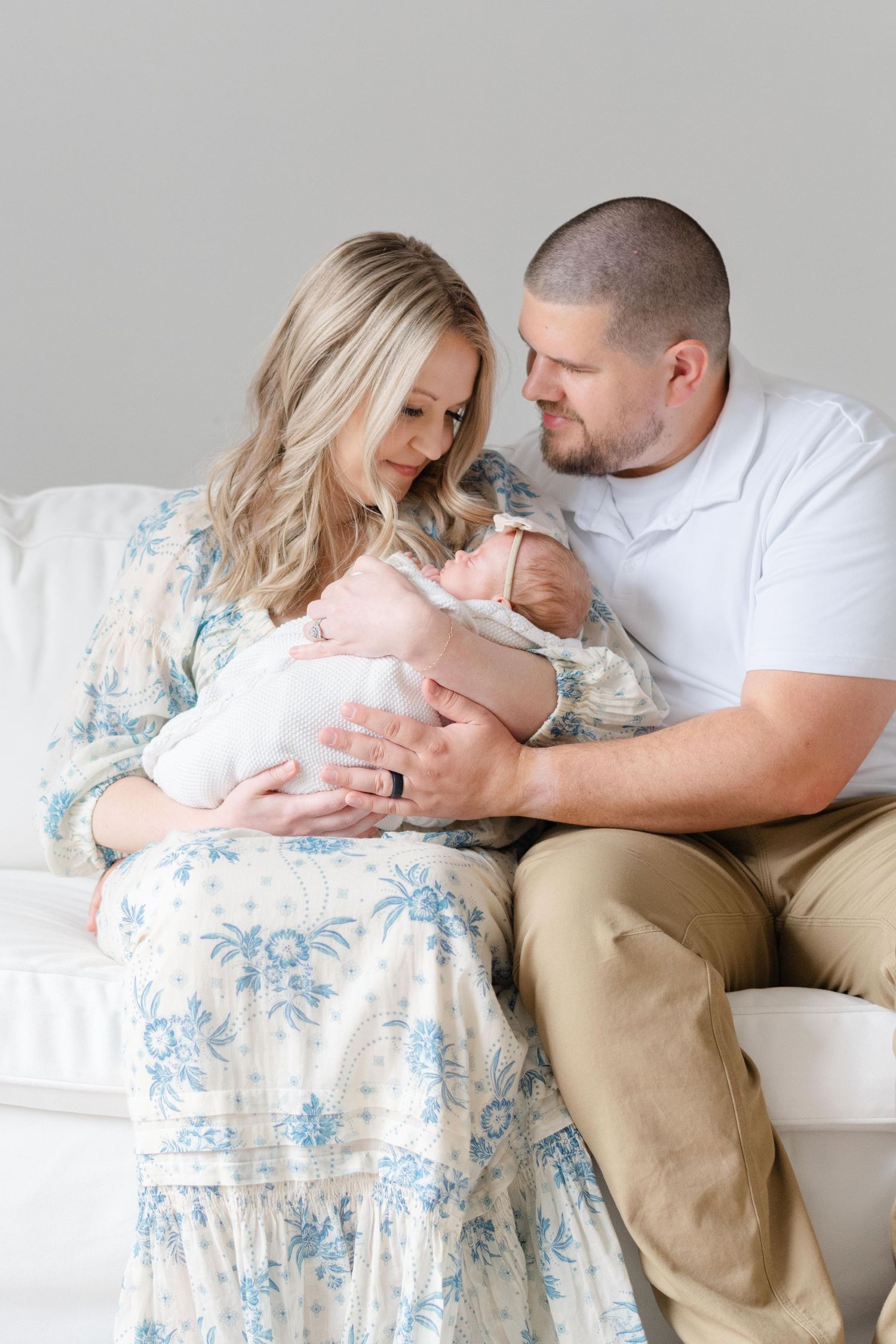 New parents holding newborn on white couch in natural light studio, Richmond newborn photographer