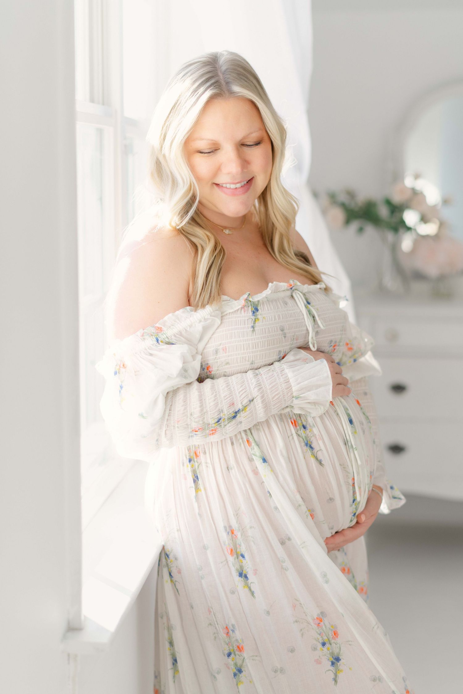 A person wearing a flowy white floral dress poses in a bright white studio setting with natural lighting.