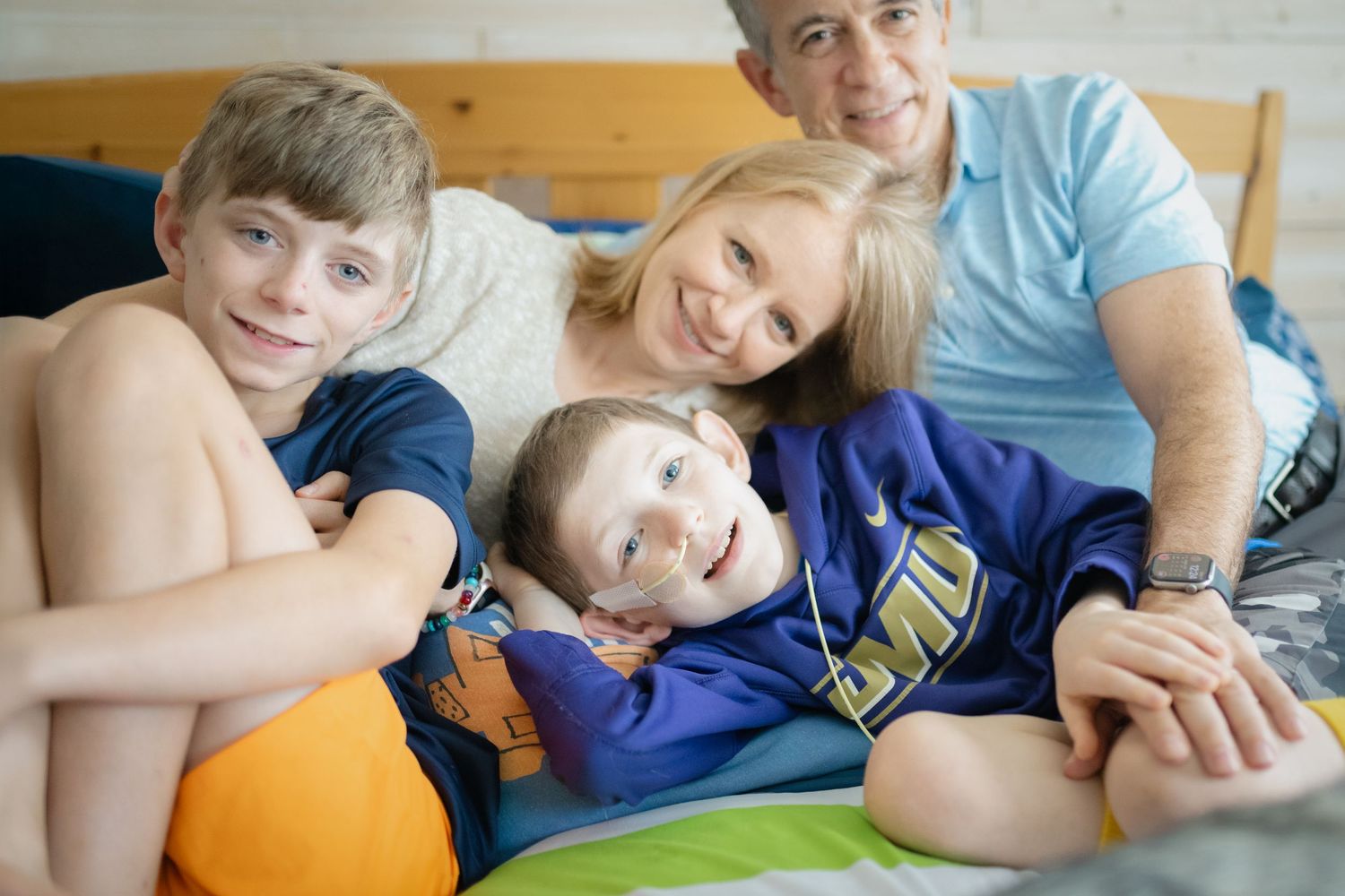 Happy family of four relaxing together on a bed, smiling warmly in a cozy bedroom setting.