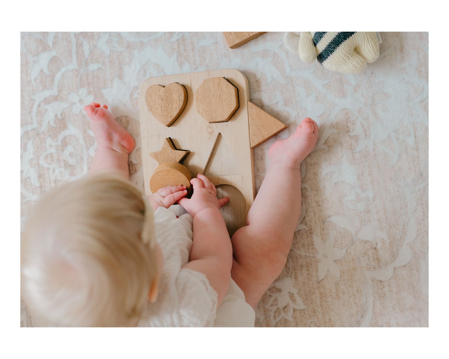 Baby's tiny feet and hands play with wooden toys on a soft white surface.
