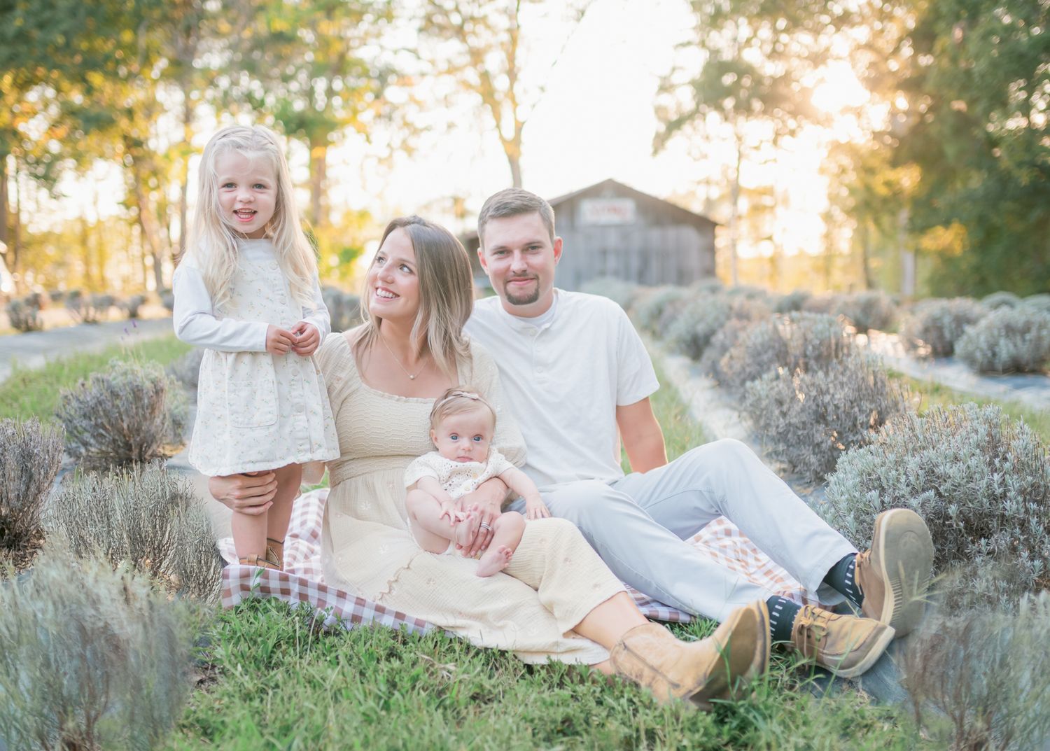 A family sits together on a blanket in a field of sagebrush during golden hour sunset.