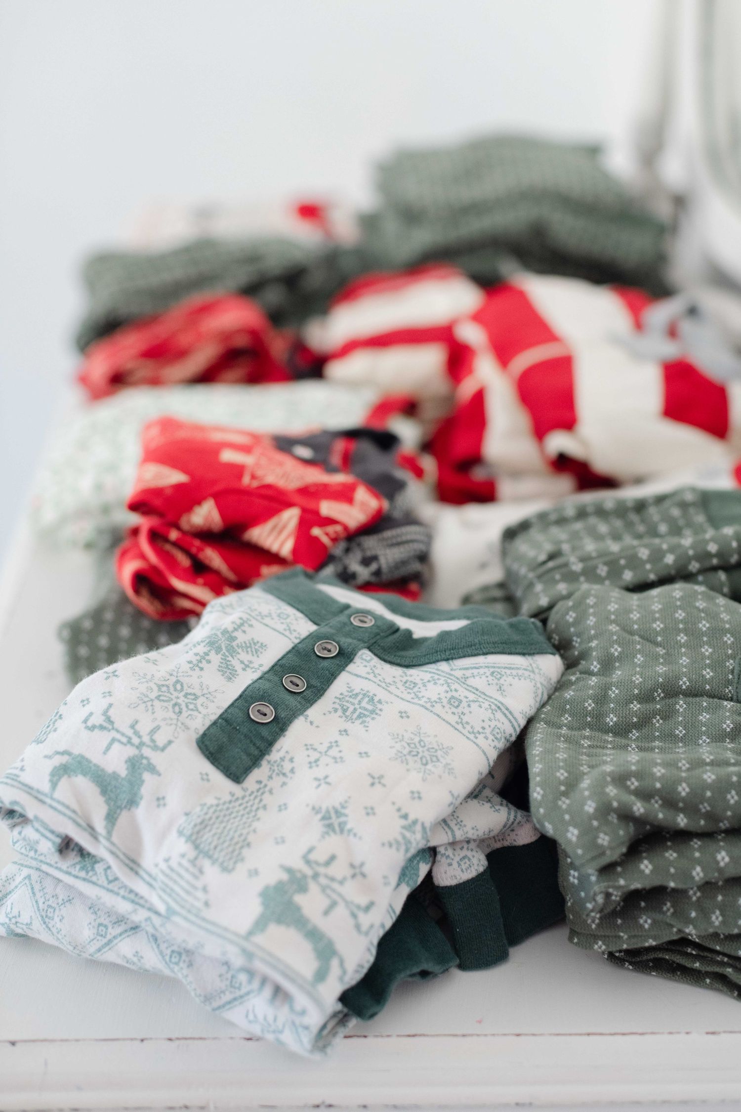Folded Christmas pajamas in festive red, green, and white patterns with reindeer and snowflake prints stacked on a white surface.