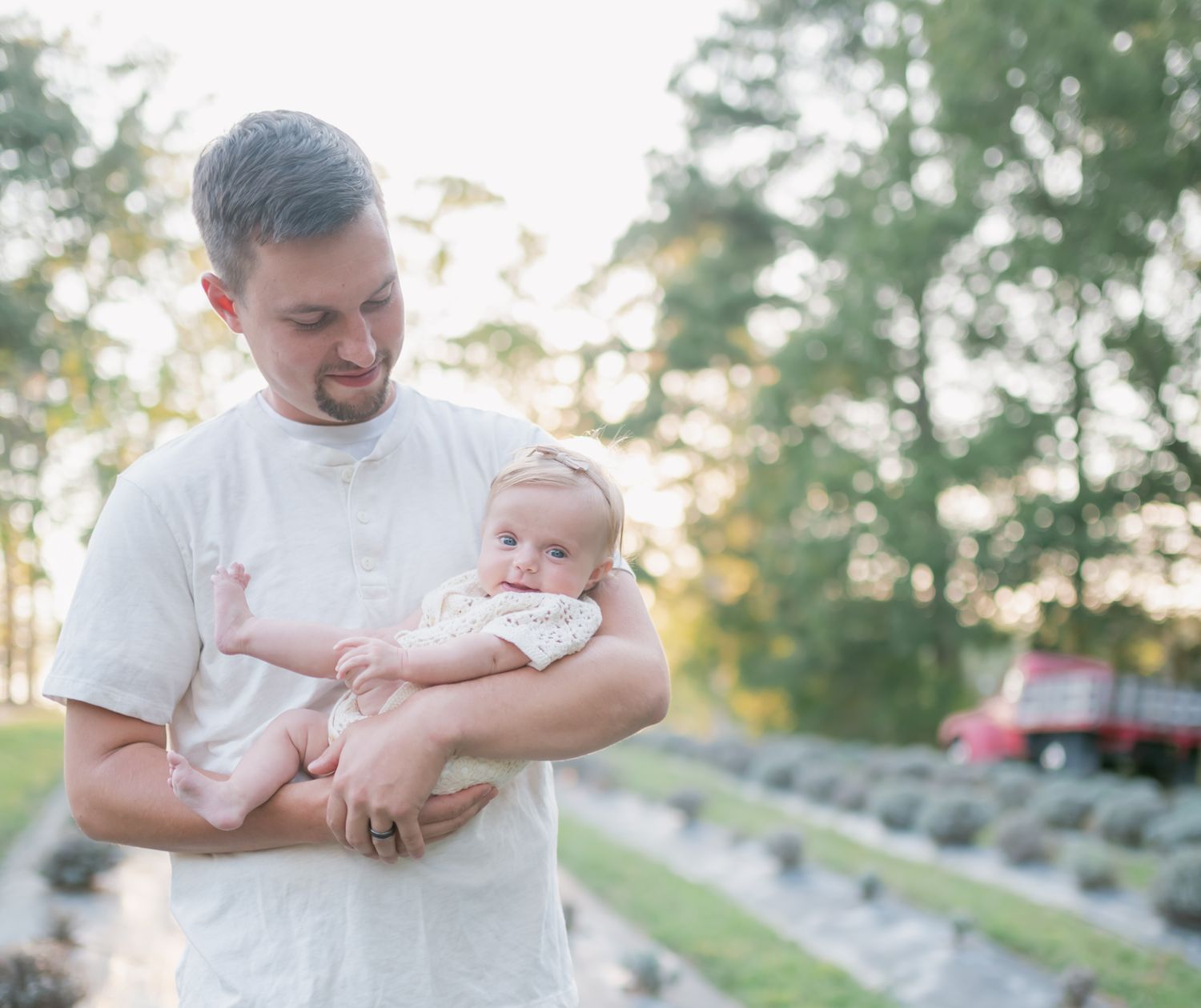 A parent in a white shirt holds and plays with a baby outdoors during golden hour.