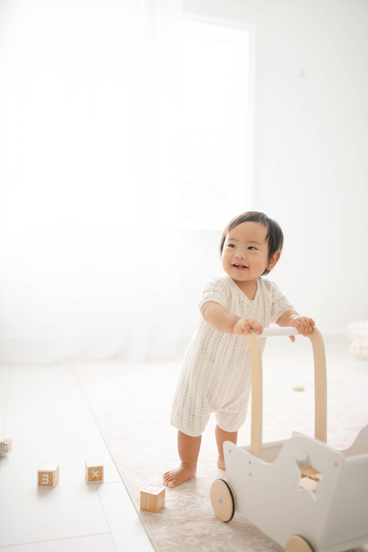 Baby in white outfit crawls and plays on light wooden floor in bright minimalist Richmond photography studio