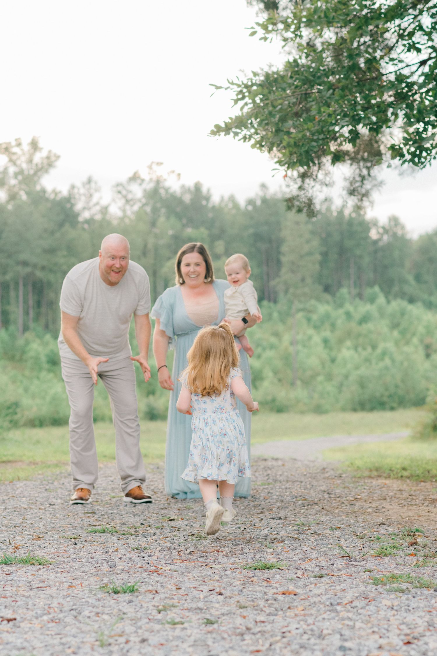 Family walking together on a gravel path surrounded by green trees and nature in soft pastel lighting.