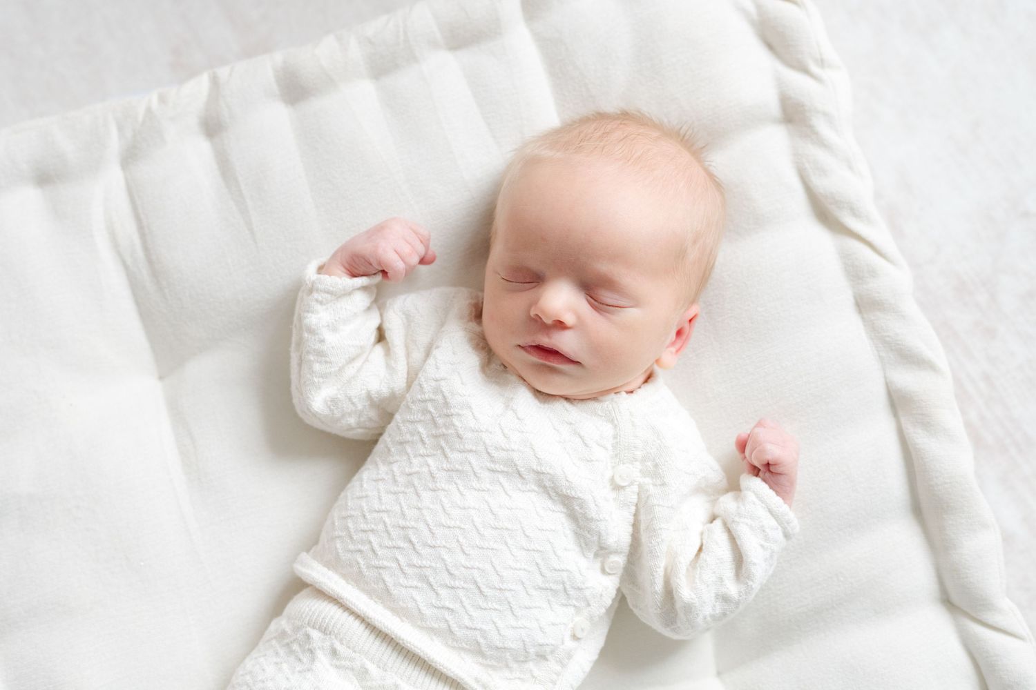 Sleeping newborn baby in soft white outfit on neutral bedding in a light filled Richmond Virginia studio