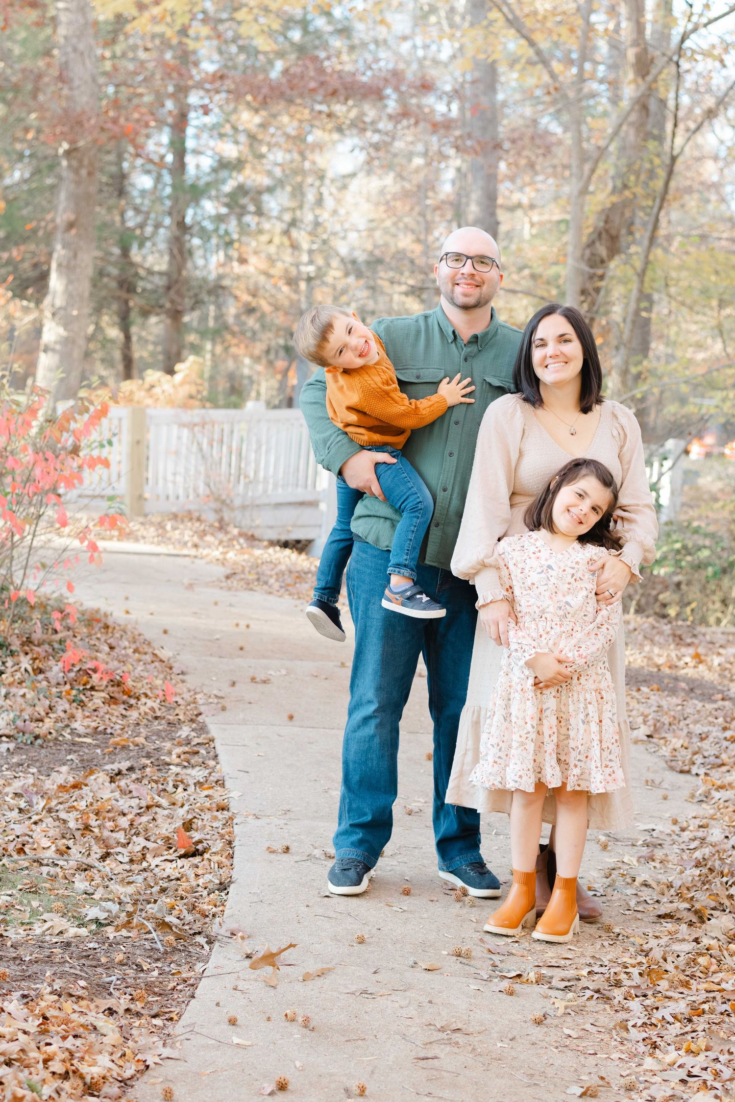 Happy family of four posing on a garden path surrounded by colorful autumn foliage and trees.
