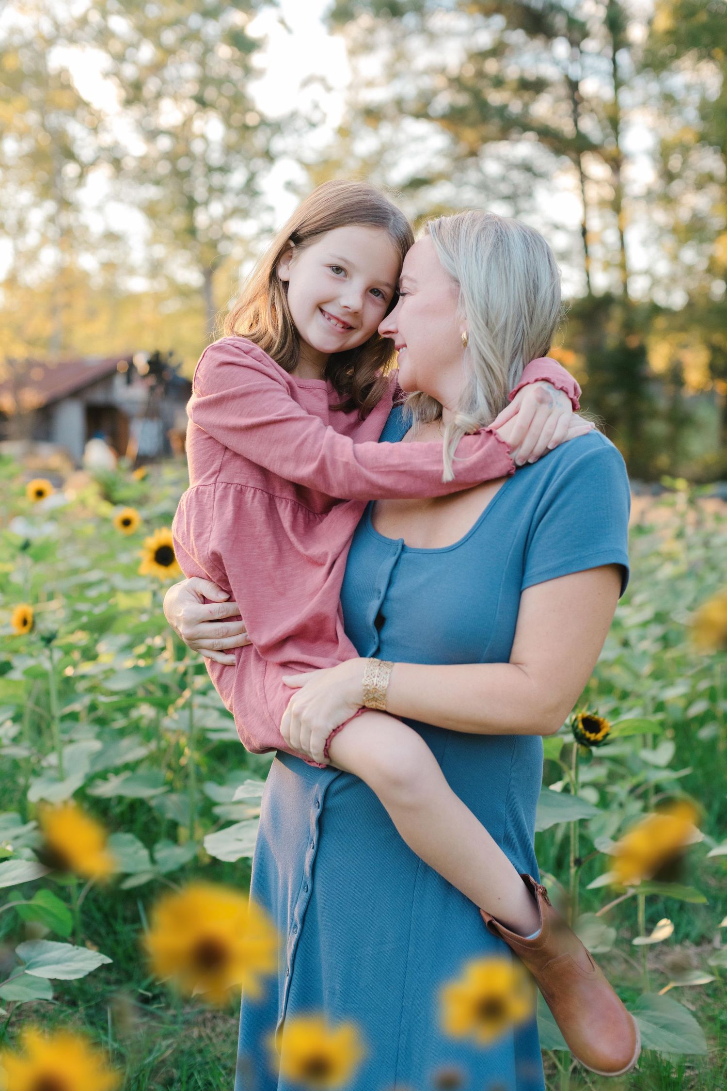 Parent and child share tender moments in a vibrant sunflower field during golden hour.
