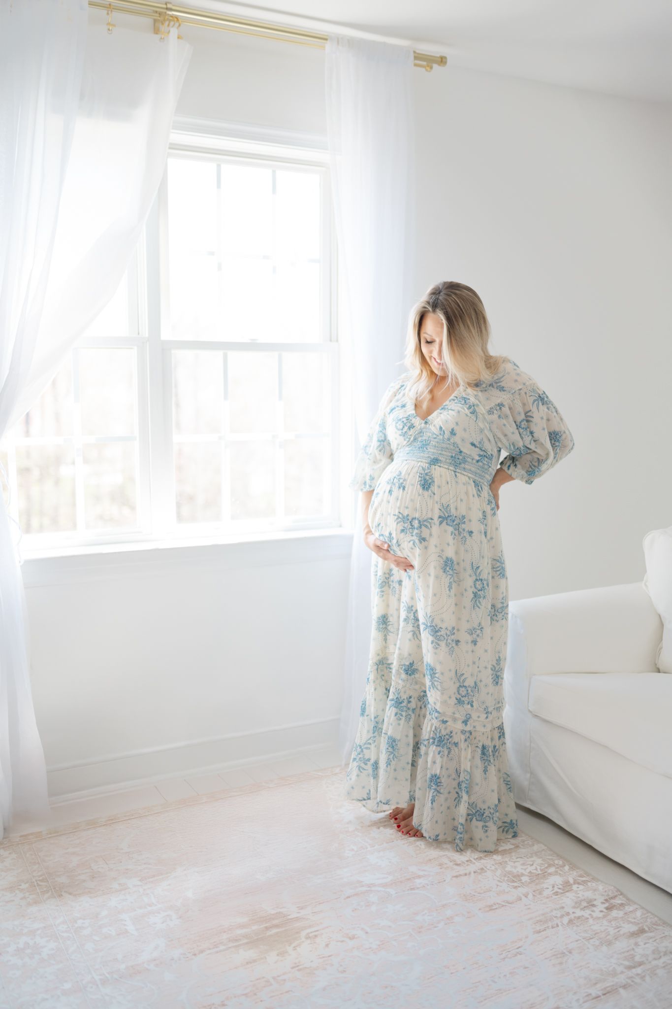 Woman in floral blue dress posing in bright white studio space.