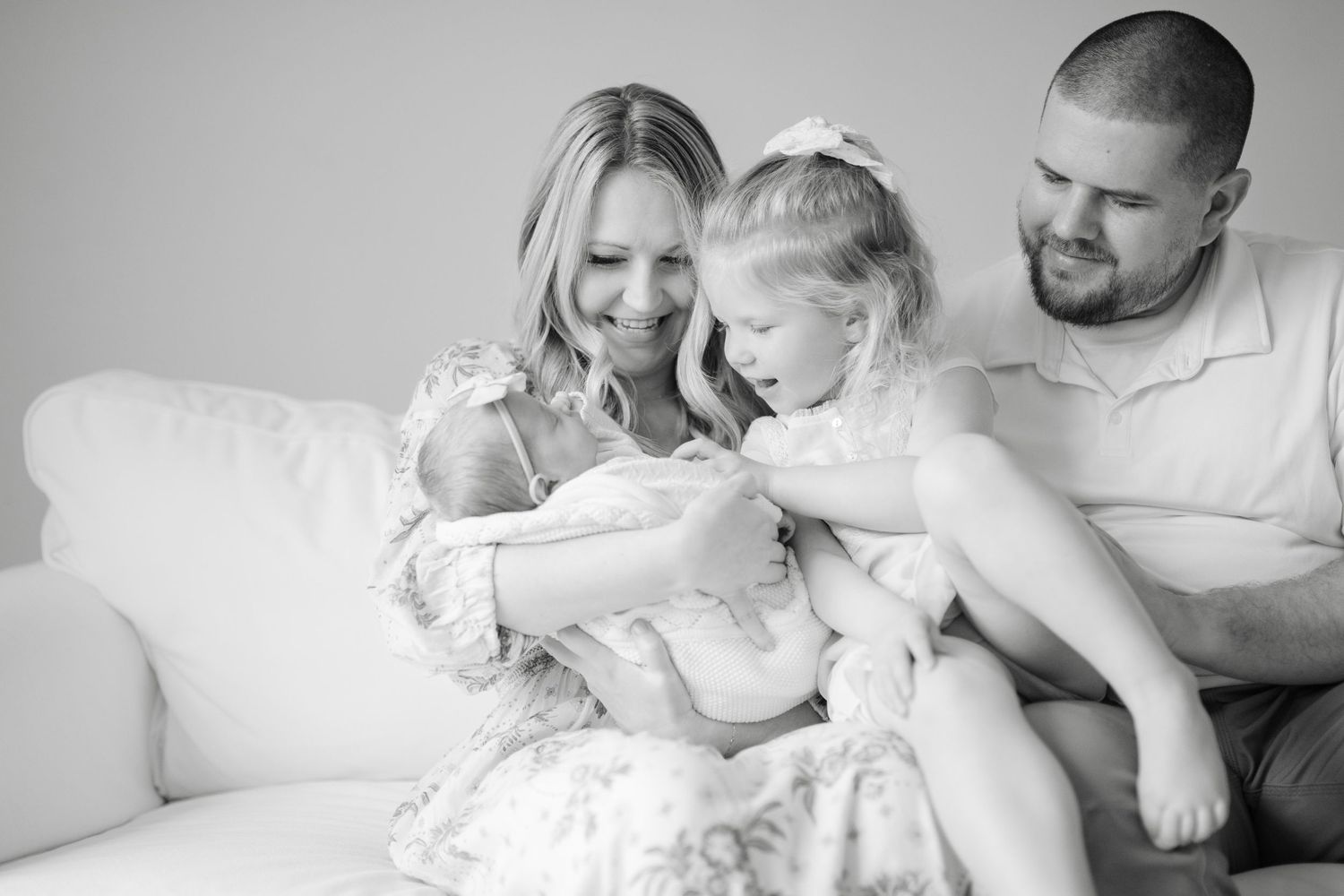 A tender black and white family portrait shows parents and child sharing intimate moments on a white couch.