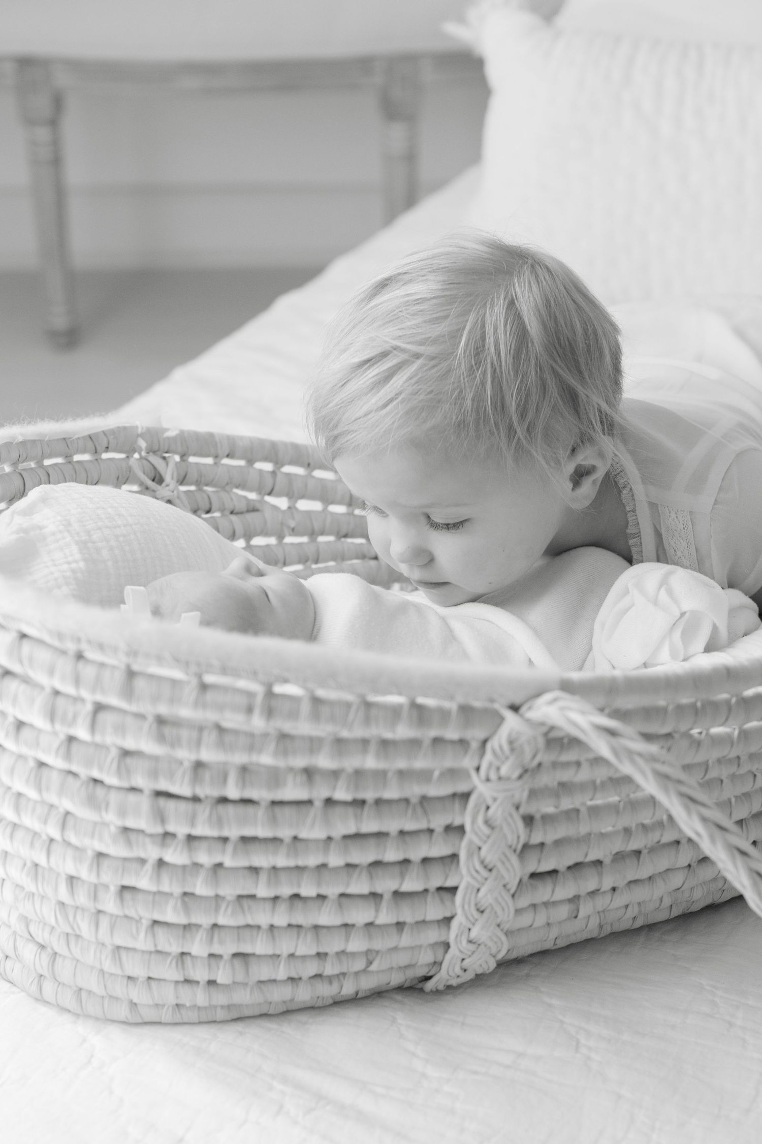 Baby sleeping peacefully in white woven moses basket on bed.