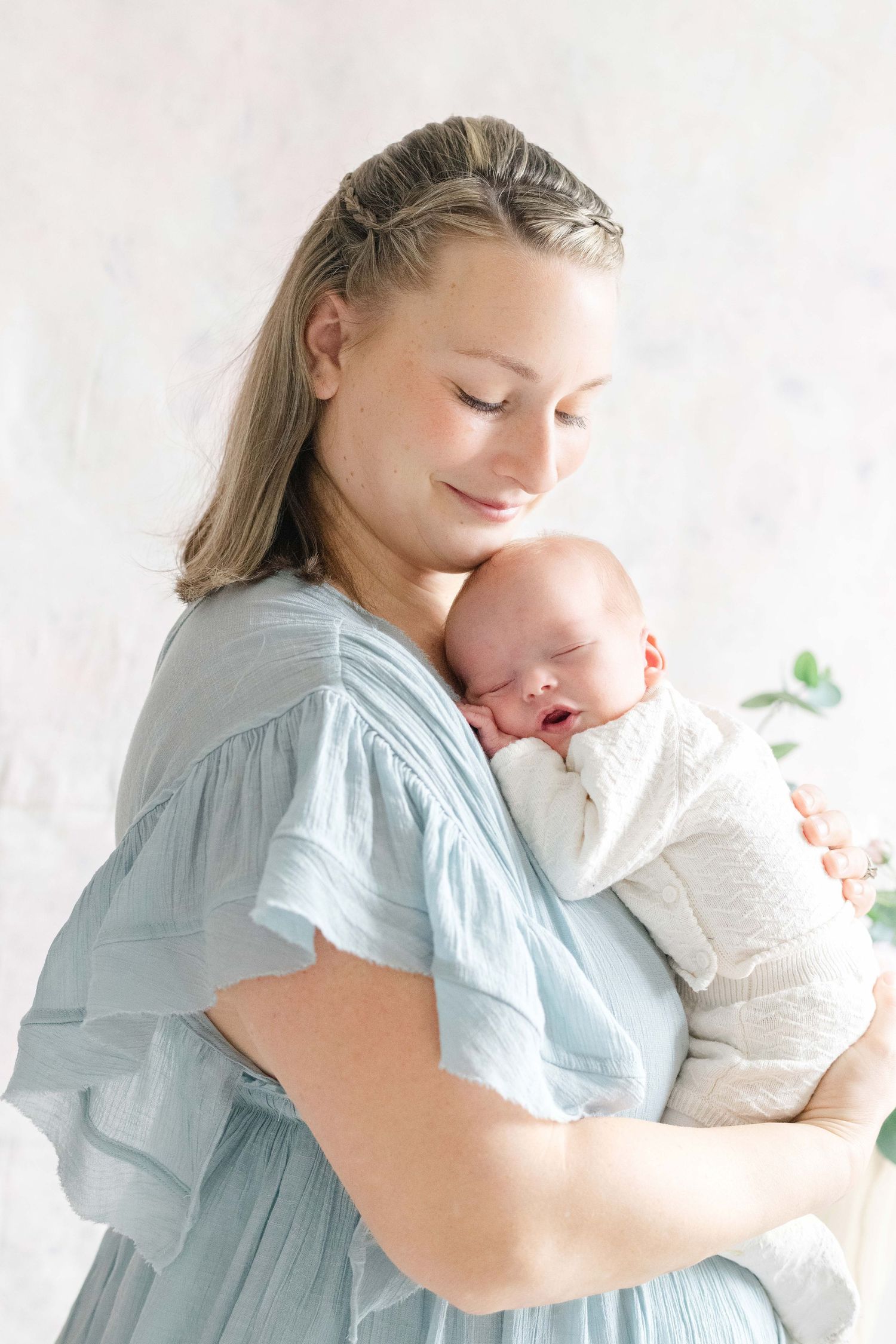 Mother in light blue dress tenderly holding sleeping newborn baby during a newborn photography session in a Chesterfield photography studio