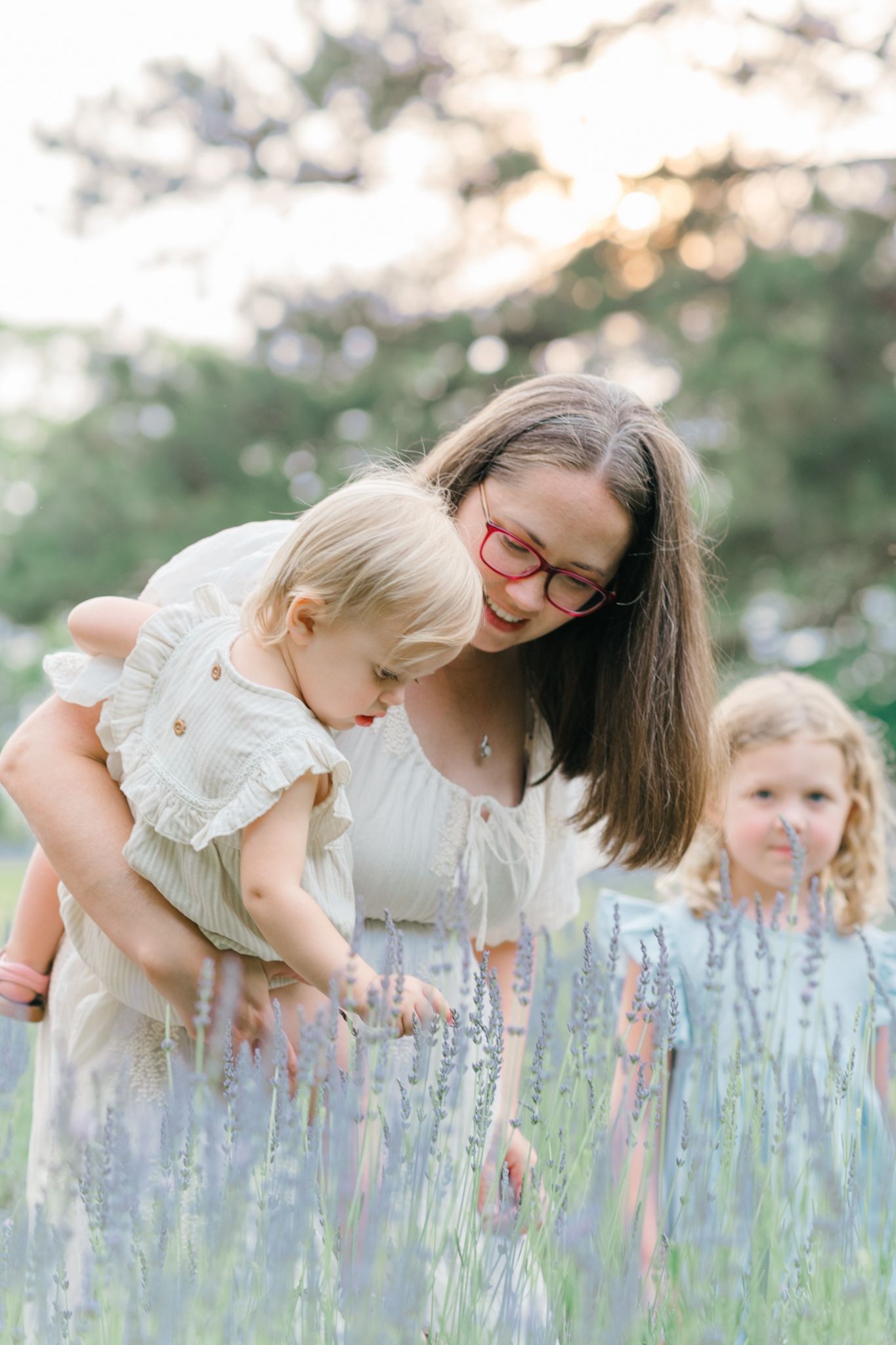 Mother and child bending down to smell purple lavender flowers in garden.