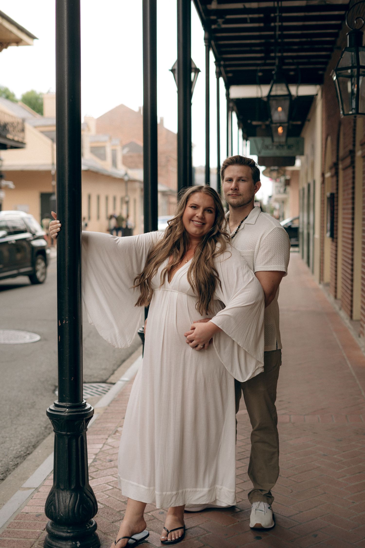 A couple poses together under a covered sidewalk with classic-style lampposts in an urban setting.