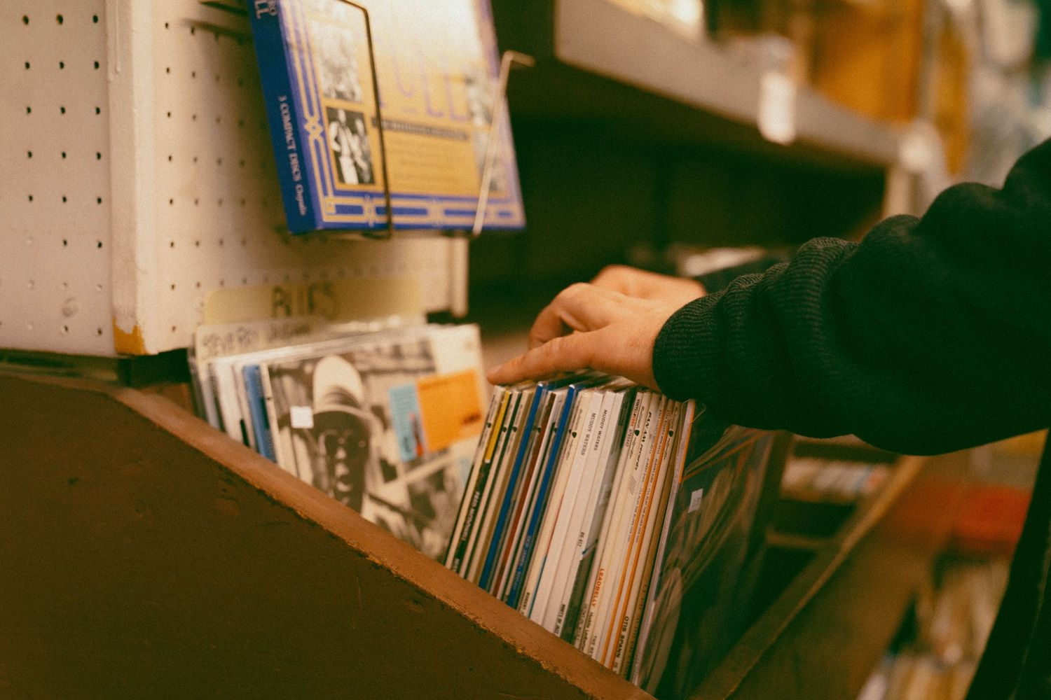Hand browsing through vinyl records in a music store collection.