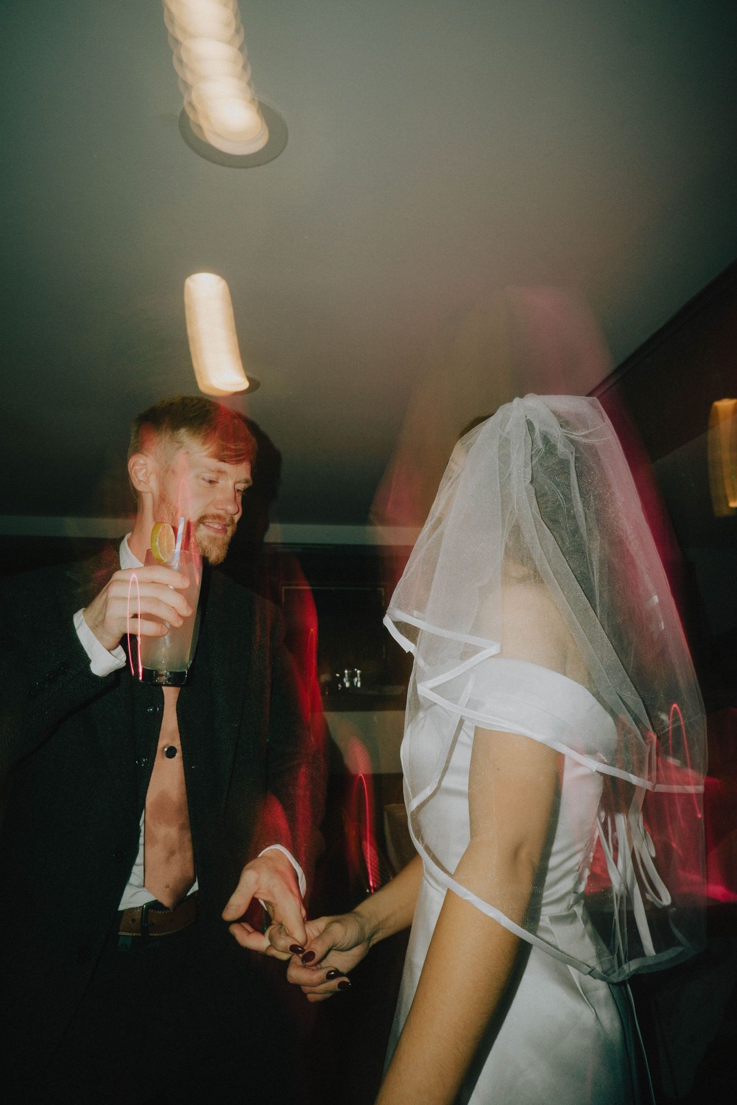 Couple holding champagne flutes dance together at their wedding celebration.