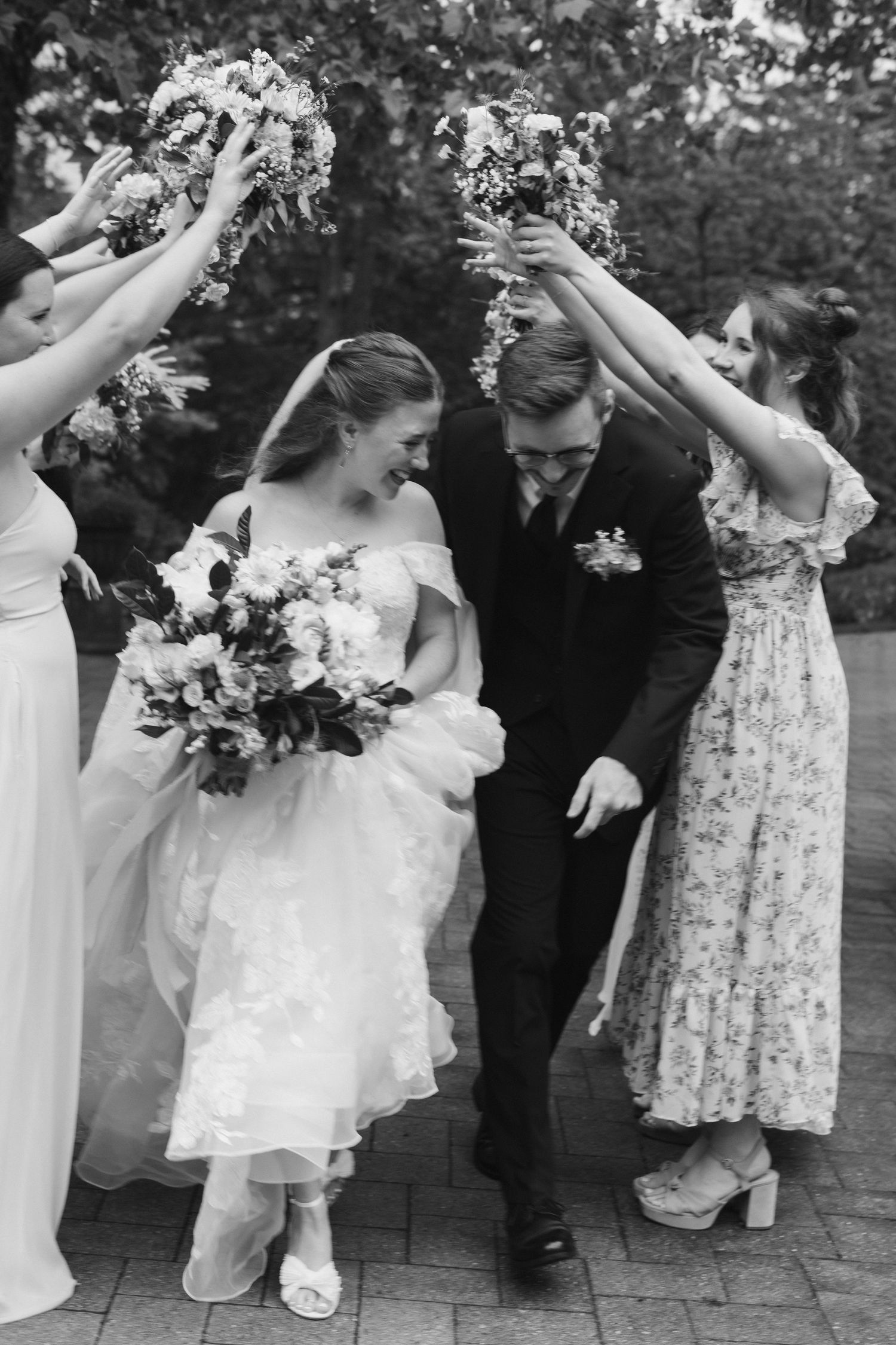 A couple celebrates under floral arches held by wedding party members during an outdoor wedding ceremony.