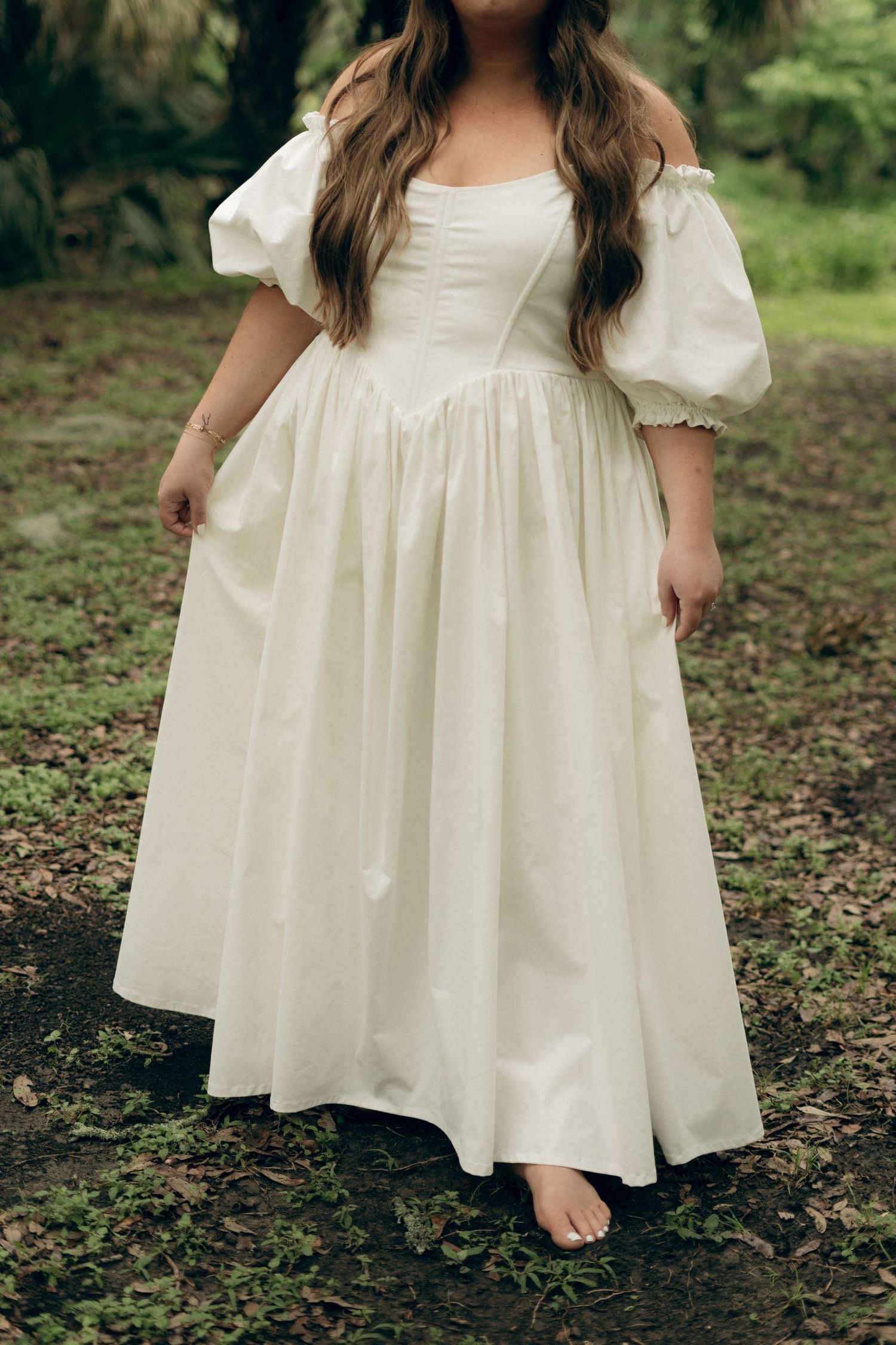 A white cotton dress with puffy sleeves and empire waist shown from different angles on a wooded ground.