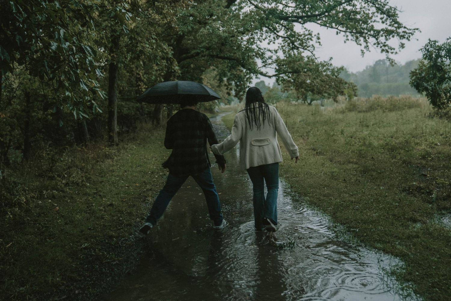 Two people walking together in rain gear along a wet path through nature.