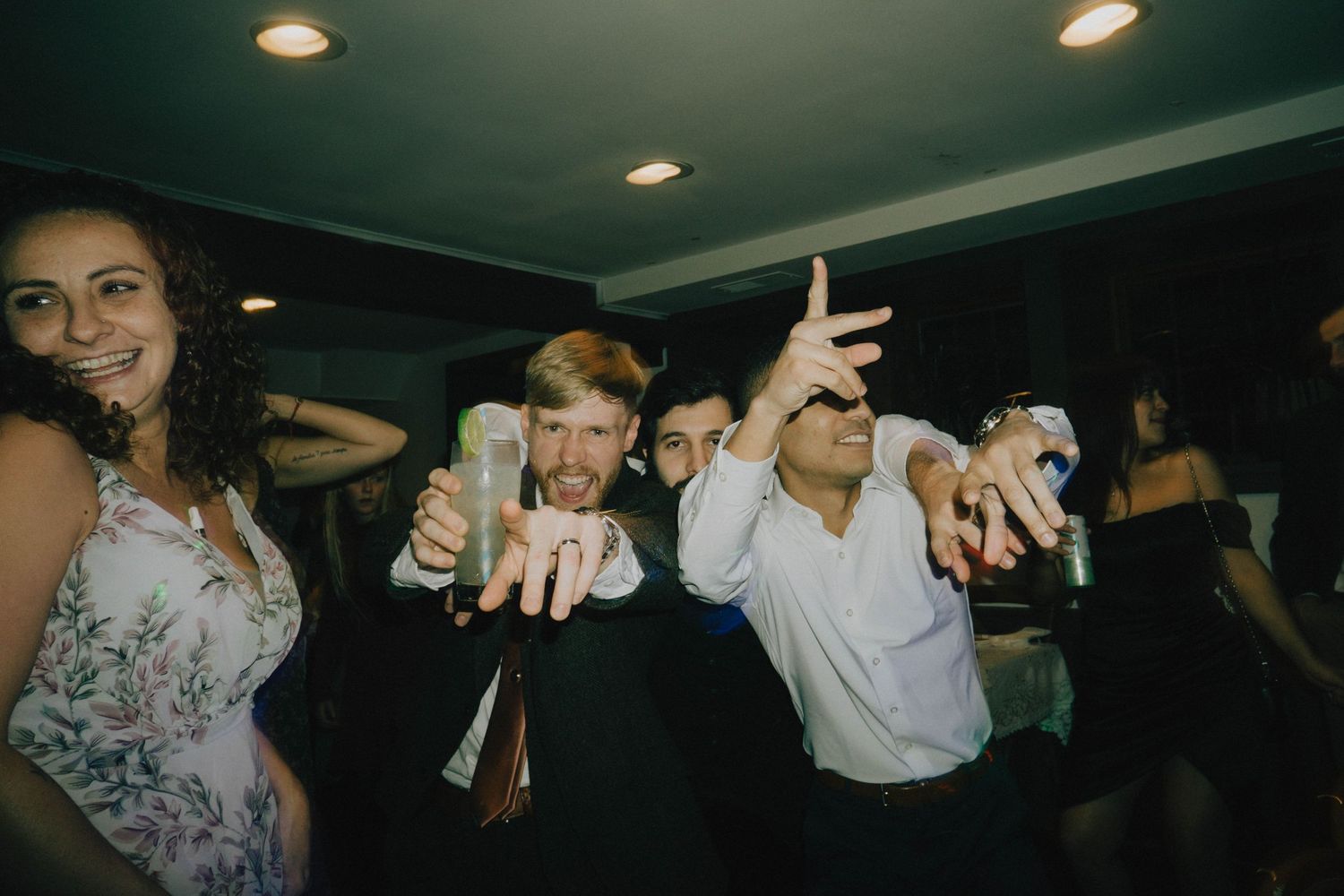 Wedding party guests dancing and celebrating with drinks on the dance floor.