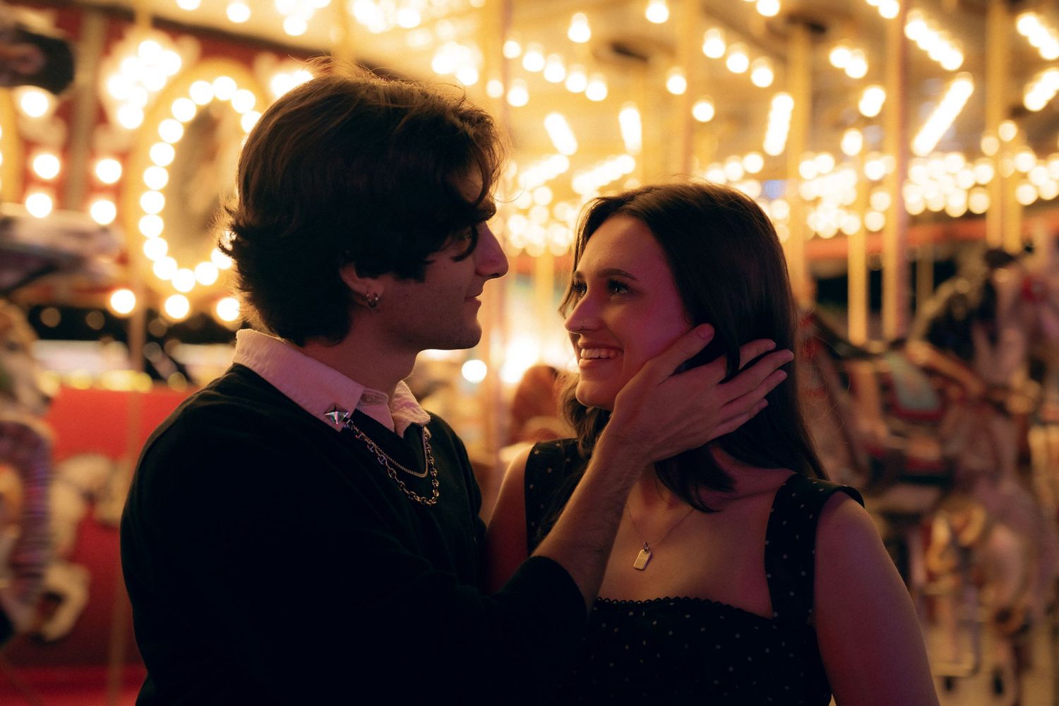 A romantic couple shares an intimate moment together at a carnival with glowing lights twinkling in the background.