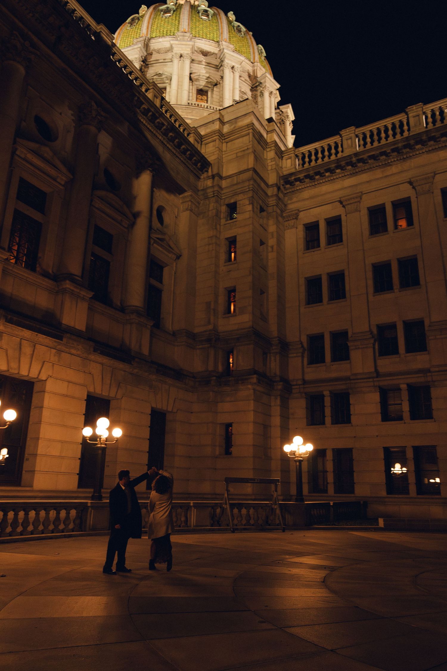 Panoramic nighttime view of an illuminated historic courtyard with ornate architecture and glowing lampposts.
