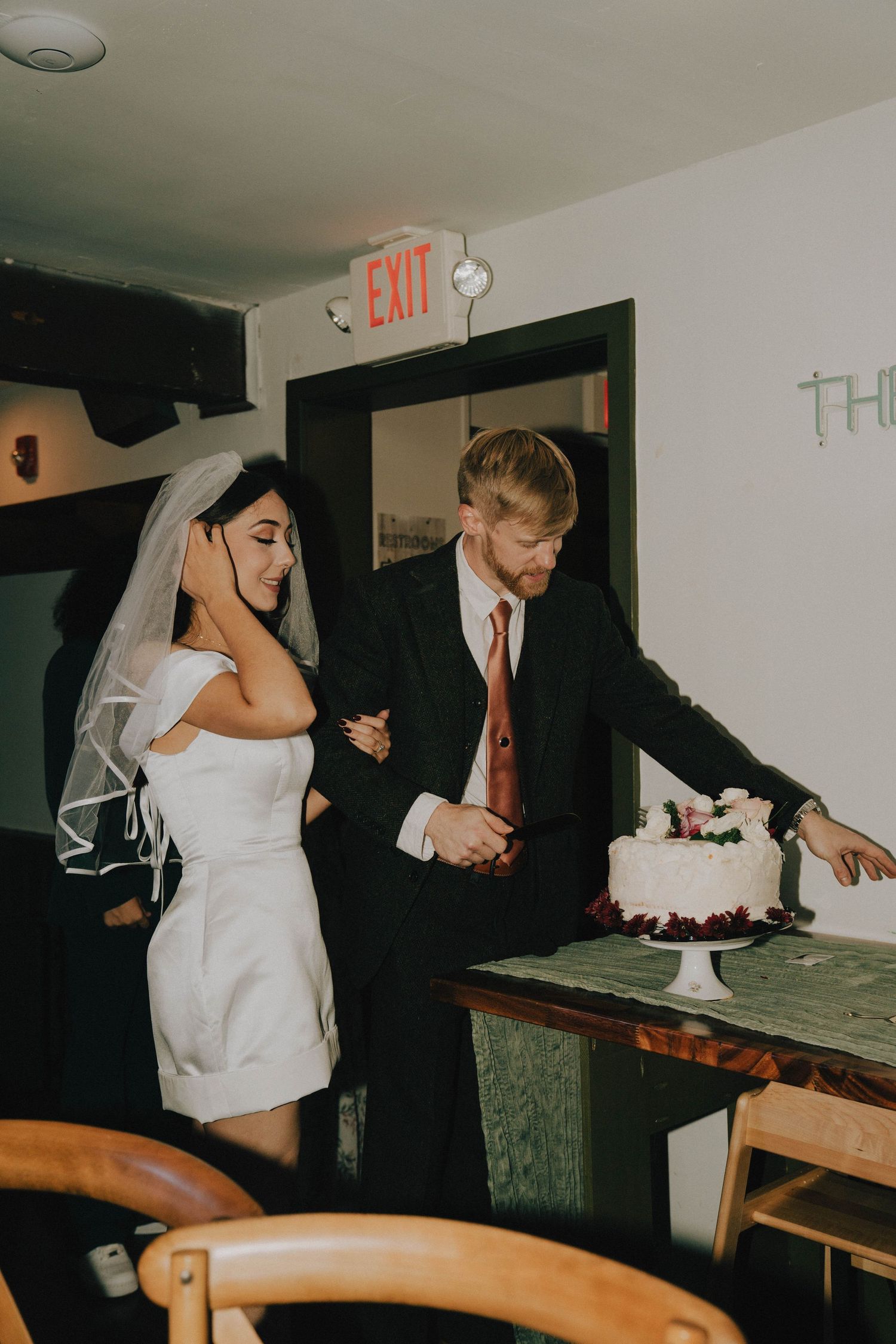 Newlyweds cutting their white wedding cake together at a reception venue.