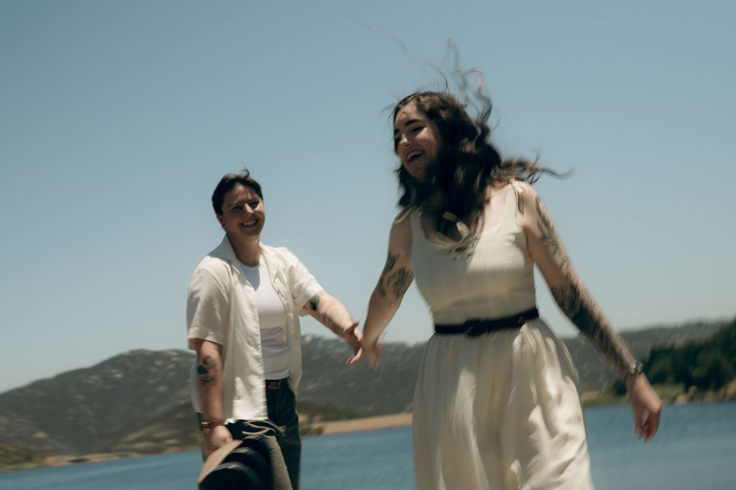 Couple running joyfully on beach with their white clothing flowing in the coastal breeze at sunset.