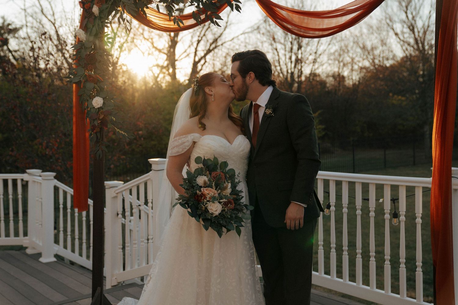 Sunset wedding ceremony under draped arch with white railing.
