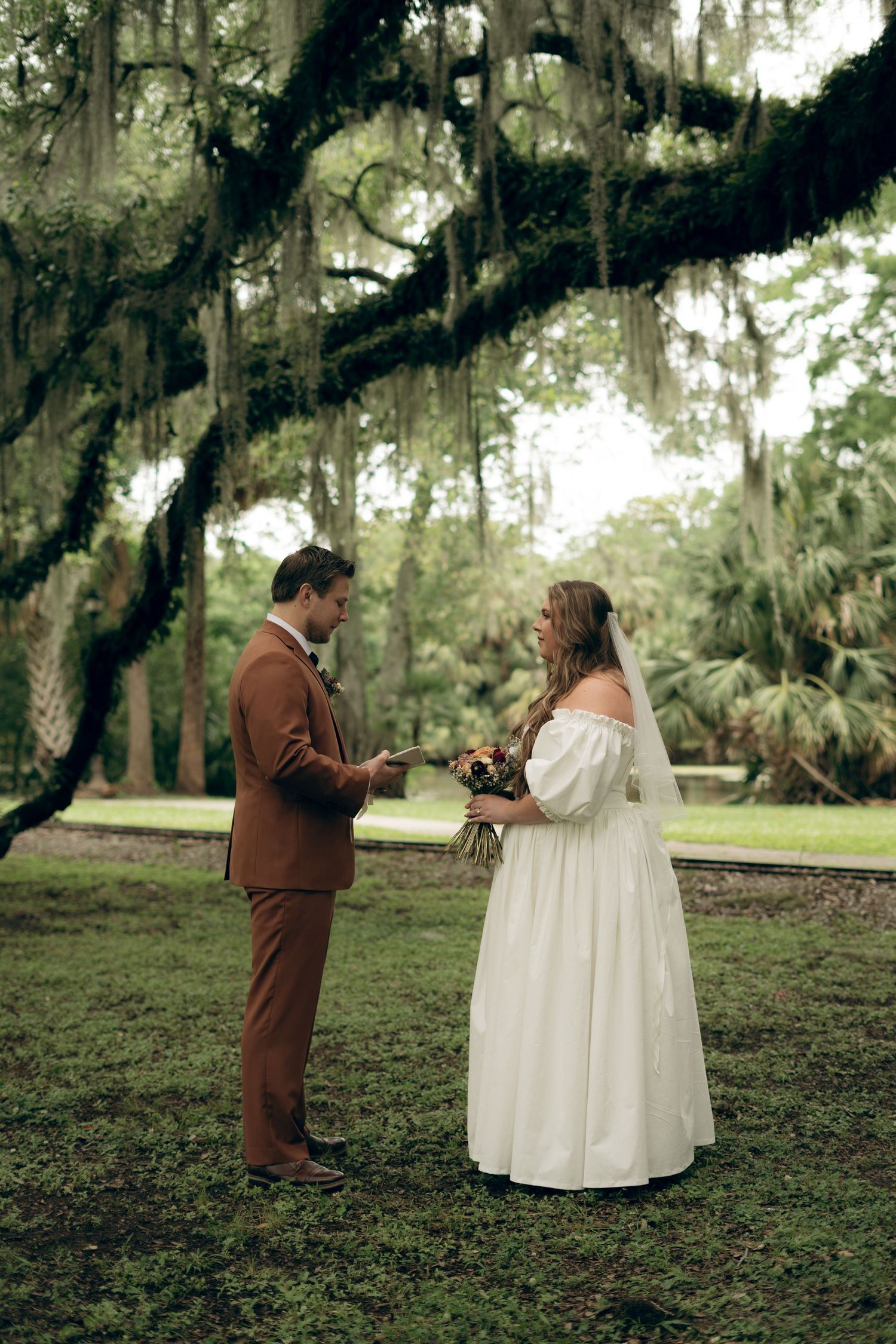 A couple exchanges wedding vows beneath Spanish moss-draped trees in a romantic outdoor ceremony.