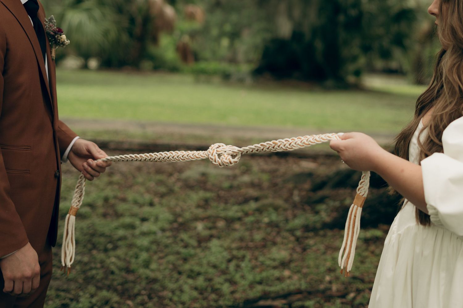 Two people hold opposite ends of a knotted rope in a green outdoor setting.