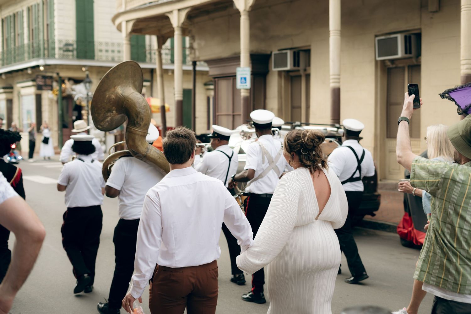 A jazz band and parade participants dance through the historic streets of New Orleans during a celebration.