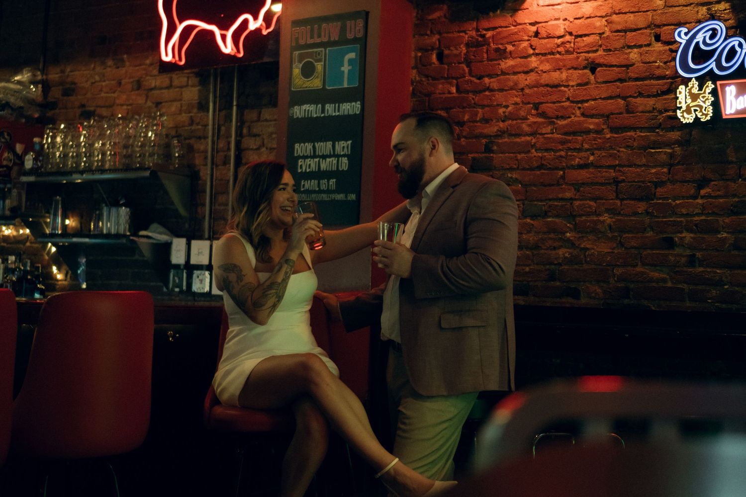 A cozy date night scene at a dimly lit bar with exposed brick walls and neon signage.