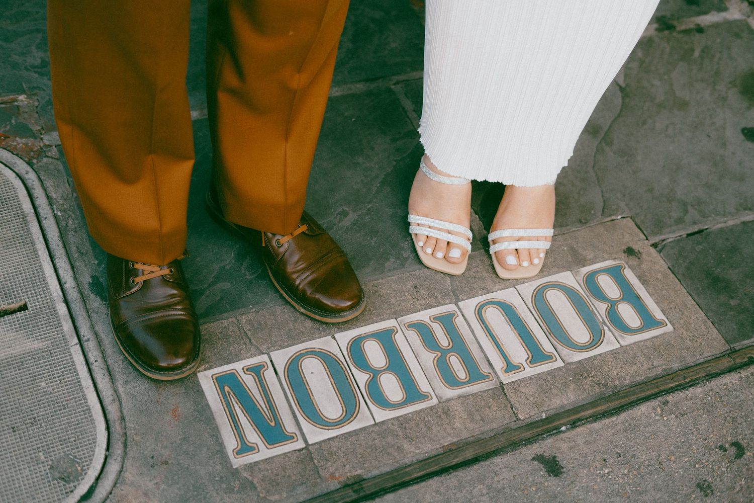 Two pairs of feet stand on a sidewalk with an upside-down BOURBON text visible on the ground.