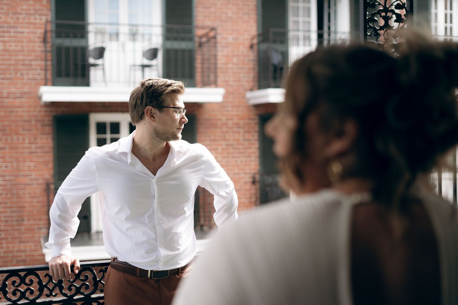 People having a conversation on a balcony with brick building exterior and white windows visible in background.