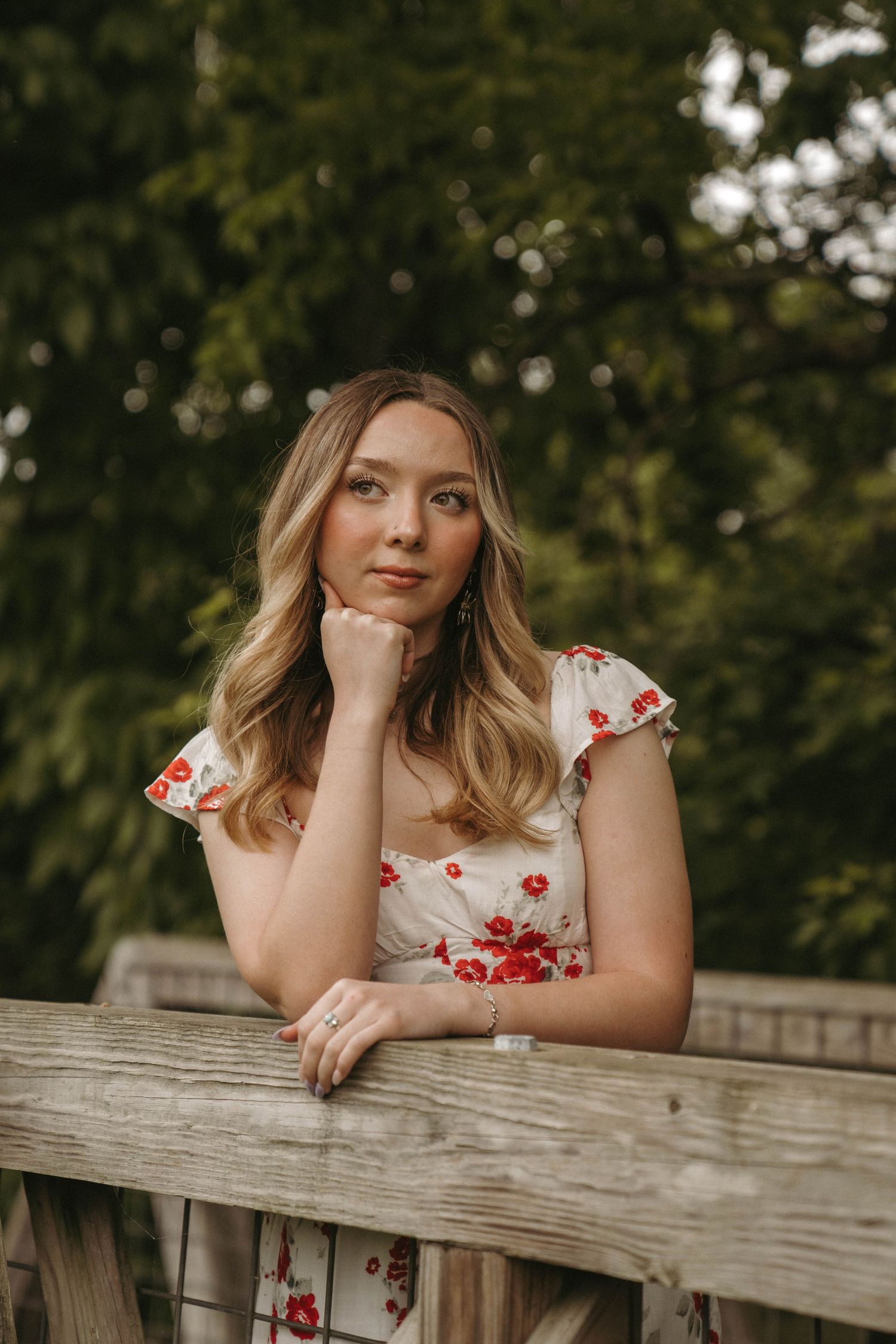 Portrait of person in floral dress leaning on wooden railing outdoors.