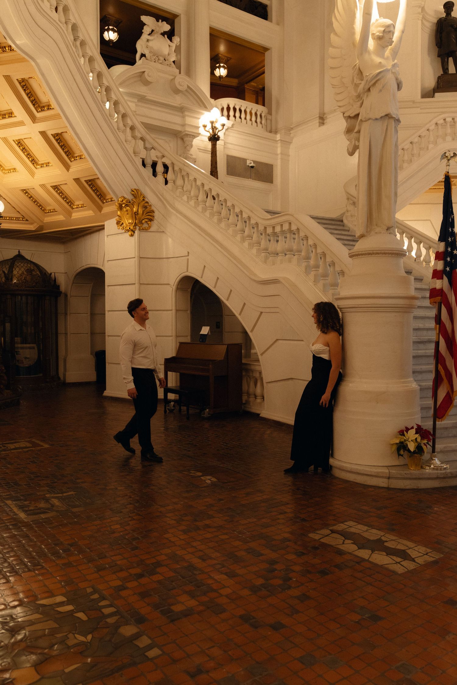 People walk through an ornate white hallway with decorative moldings and a dark tiled floor in an elegant building.