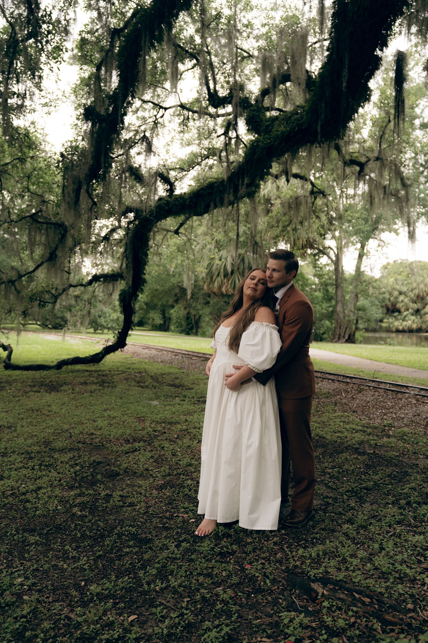 A couple shares an intimate moment under Spanish moss-draped trees in a romantic outdoor setting. New Orleans