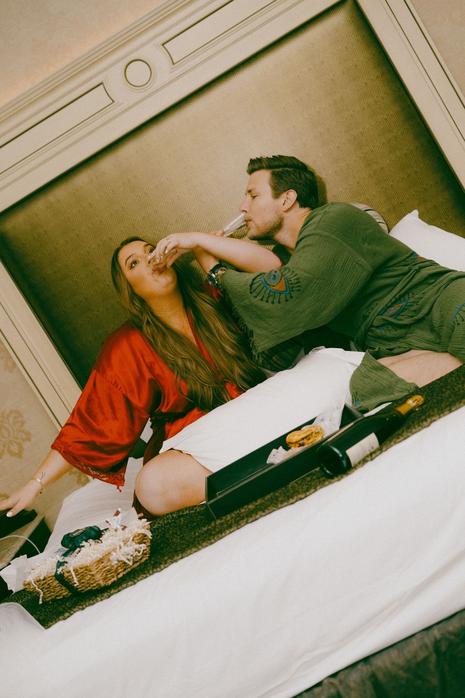 Two figures in casual clothing lying on a carpeted floor and laughing together.